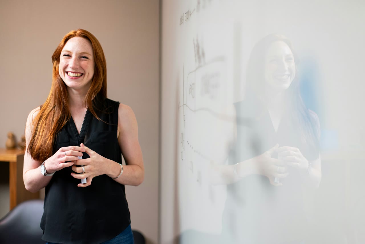 An Irish primary teacher smiling beside a whiteboard
